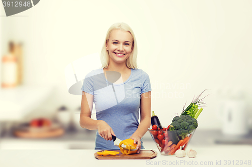 Image of smiling young woman chopping vegetables on kitchen
