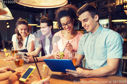 Image of happy friends with tablet pc and drinks at bar