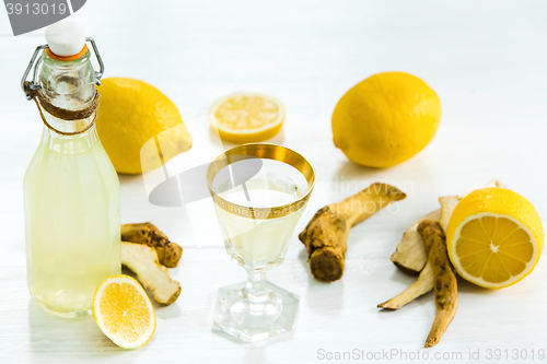 Image of Home ginger tincture in a glass and fresh lemons on the white wooden background