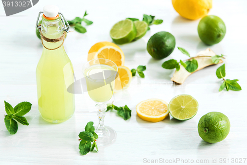 Image of Home lime liquor in a glass and fresh lemons, limes on the white wooden background