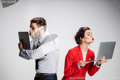 Image of The young businessman and businesswoman with laptops kissing screens on gray background