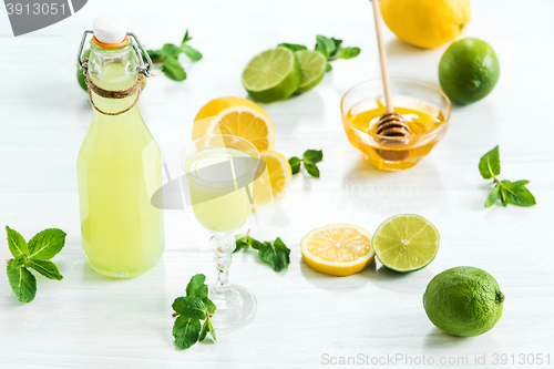Image of Home lime liquor in a glass and fresh lemons, limes on the white wooden background