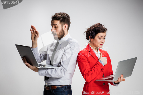 Image of The young businessman and businesswoman with laptops communicating on gray background