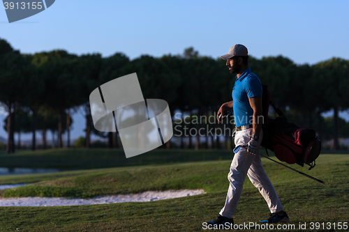 Image of golfer  walking and carrying golf  bag at beautiful sunset