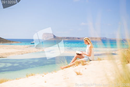 Image of Woman reading book, enjoying sun on beach.