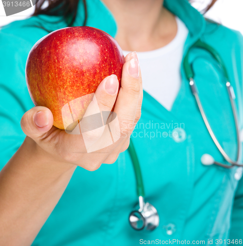 Image of Young lady doctor is holding a red apple