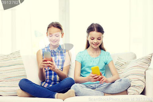 Image of happy girls with smartphones sitting on sofa