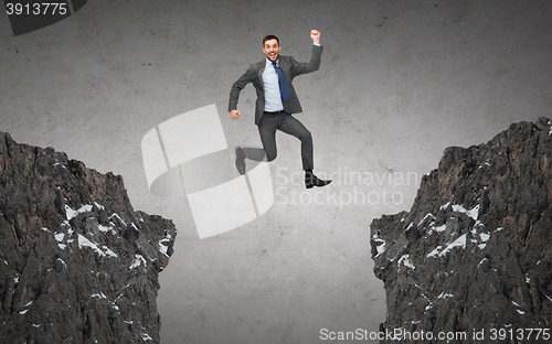 Image of happy smiling businessman jumping between rocks