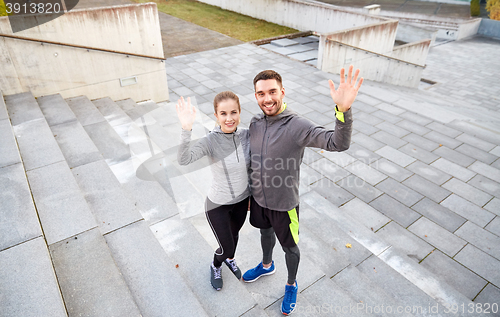 Image of happy couple waving hands outdoors on city street
