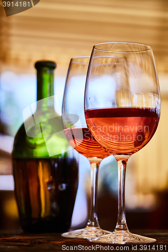 Image of two glasses filled with red wine and bottle in background