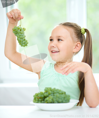 Image of Cute little girl is looking at green grapes