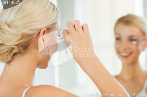 Image of woman fixing makeup with cotton swab at bathroom