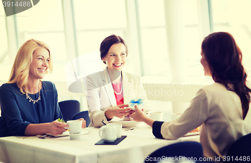 Image of happy women giving birthday present at restaurant