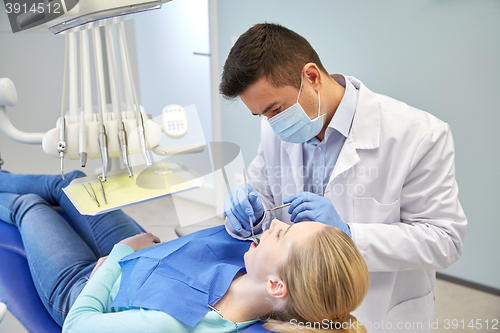 Image of male dentist in mask checking female patient teeth