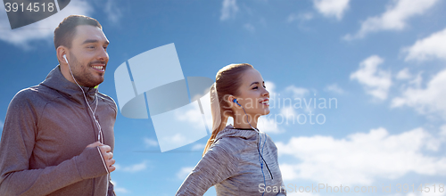 Image of happy couple with earphones running over blue sky