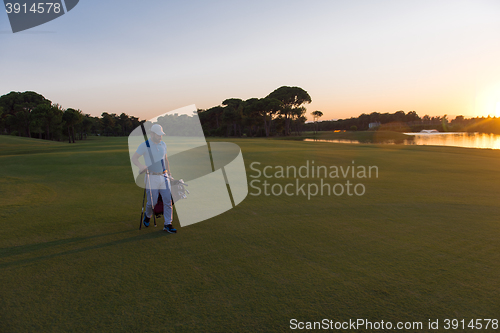 Image of golfer  walking and carrying golf  bag at beautiful sunset