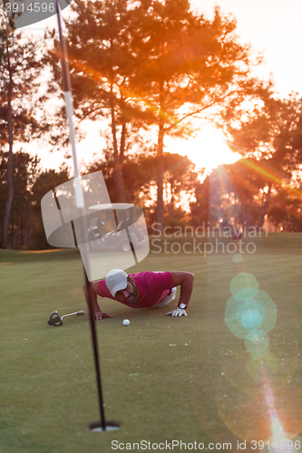 Image of golf player blowing ball in hole with sunset in background