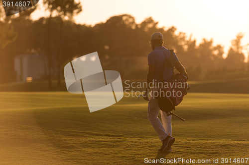 Image of golfer  walking and carrying golf  bag at beautiful sunset