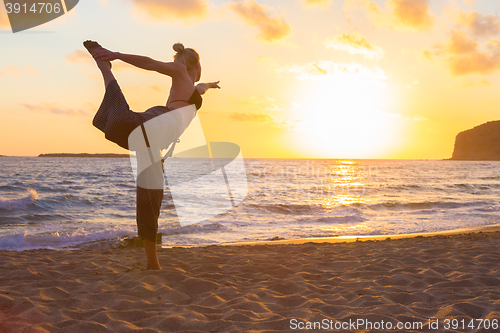 Image of Woman practicing yoga on sea beach at sunset.