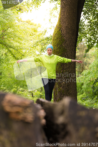 Image of Woman holding balance on tree trunk in nature.