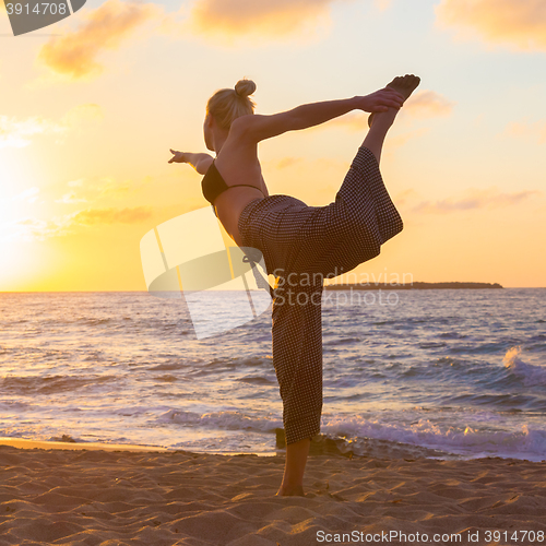 Image of Woman practicing yoga on sea beach at sunset.