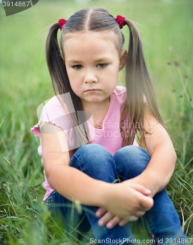 Image of Sad little girl is sitting on green grass