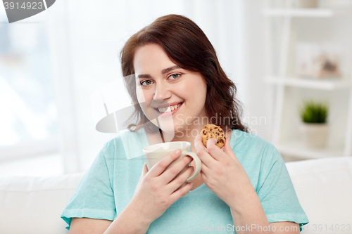 Image of happy plus size woman with cup and cookie at home