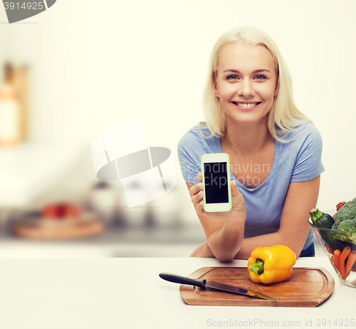 Image of smiling woman with smartphone cooking vegetables