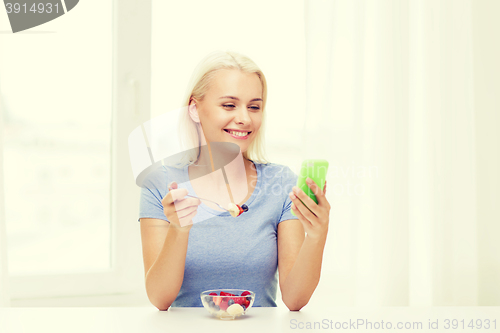 Image of woman with smartphone eating fruits at home