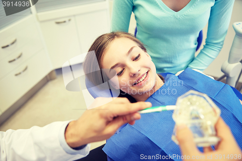 Image of happy dentist showing toothbrush to patient girl