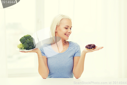 Image of smiling woman with broccoli and donut at home