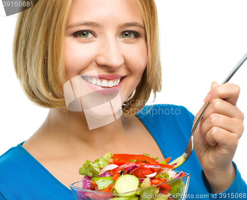 Image of Young attractive woman is eating salad using fork