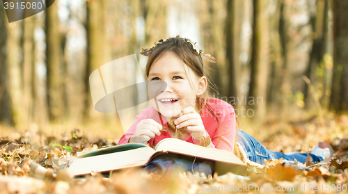 Image of Little girl is reading a book outdoors