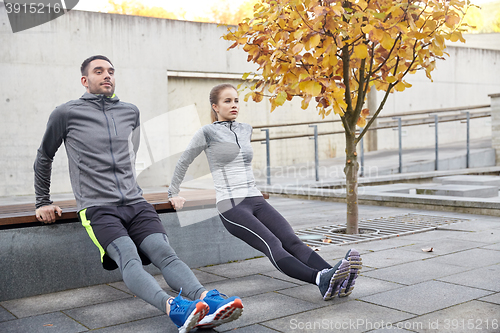 Image of couple doing triceps dip on city street bench
