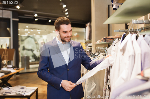 Image of happy young man choosing clothes in clothing store