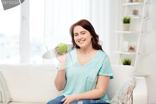 Image of happy plus size woman eating green apple at home