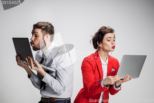 Image of The young businessman and businesswoman with laptops kissing screens on gray background