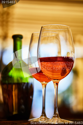 Image of two glasses filled with red wine and bottle in background