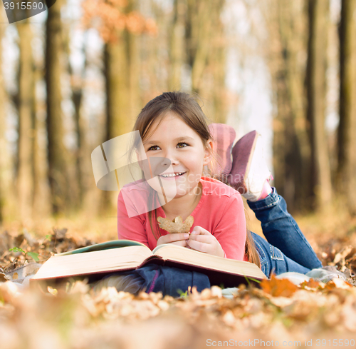 Image of Little girl is reading a book outdoors