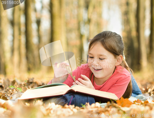 Image of Little girl is reading a book outdoors
