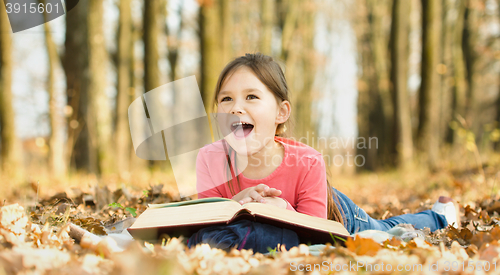 Image of Little girl is reading a book outdoors