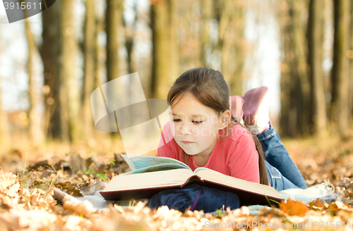 Image of Little girl is reading a book outdoors