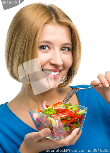 Image of Young attractive woman is eating salad using fork