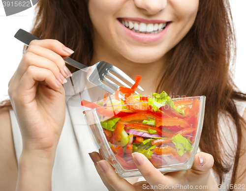 Image of Young attractive woman is eating salad using fork