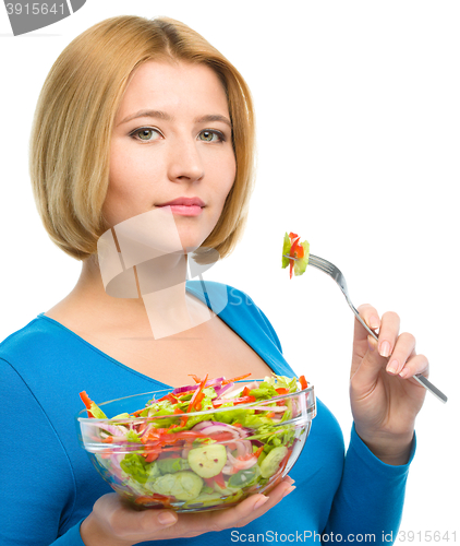 Image of Young attractive woman is eating salad using fork