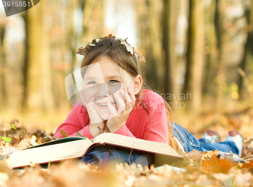 Image of Little girl is reading a book outdoors