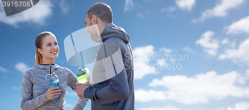 Image of smiling couple with bottles of water over blue sky