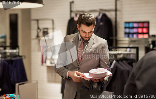 Image of happy young man choosing shirt in clothing store