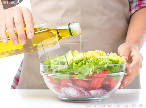 Image of Cook is pouring olive oil into salad