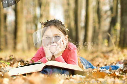 Image of Little girl is reading a book outdoors